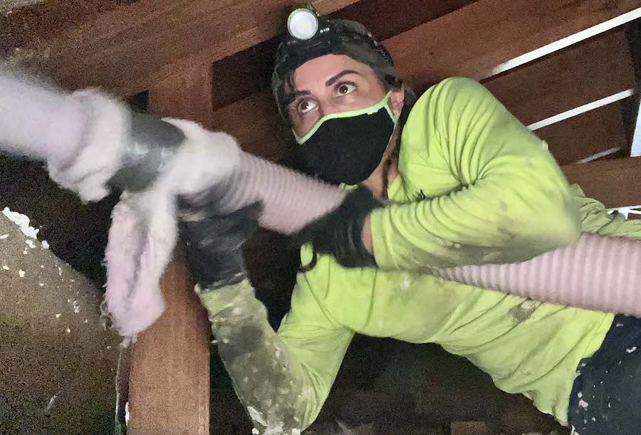 A photo of a woman holding a hose in an attic.